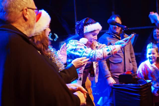 Jade Cook, founder and director of Spectrum Community Arts, presses the button to turn on the 2025 lights.