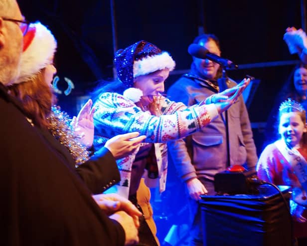 Jade Cook, founder and director of Spectrum Community Arts, presses the button to turn on the 2025 lights.